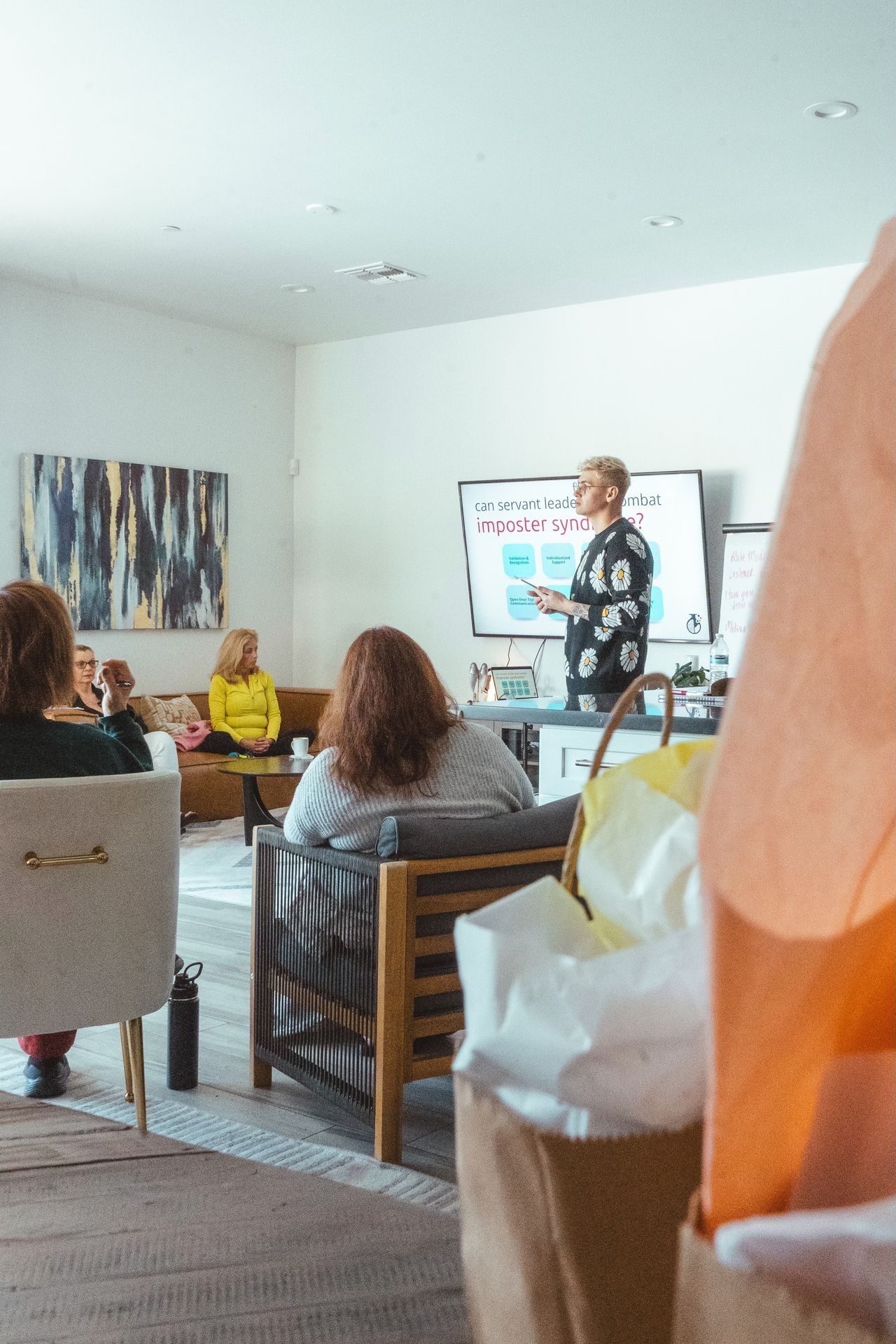 Person giving a presentation on imposter syndrome to a seated audience in a modern room.