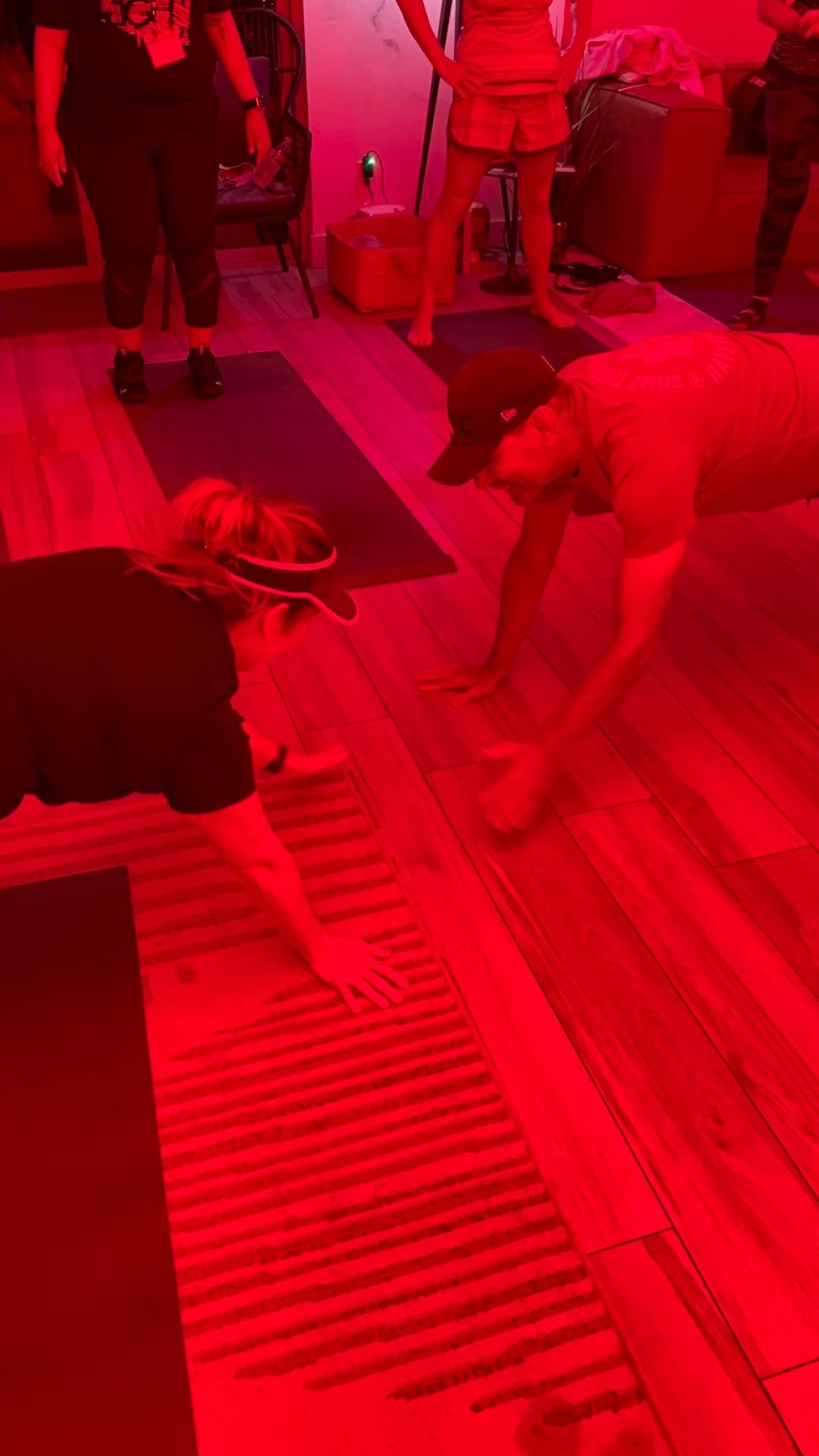 Two people high-fiving on the floor during a workout in a room with red lighting.