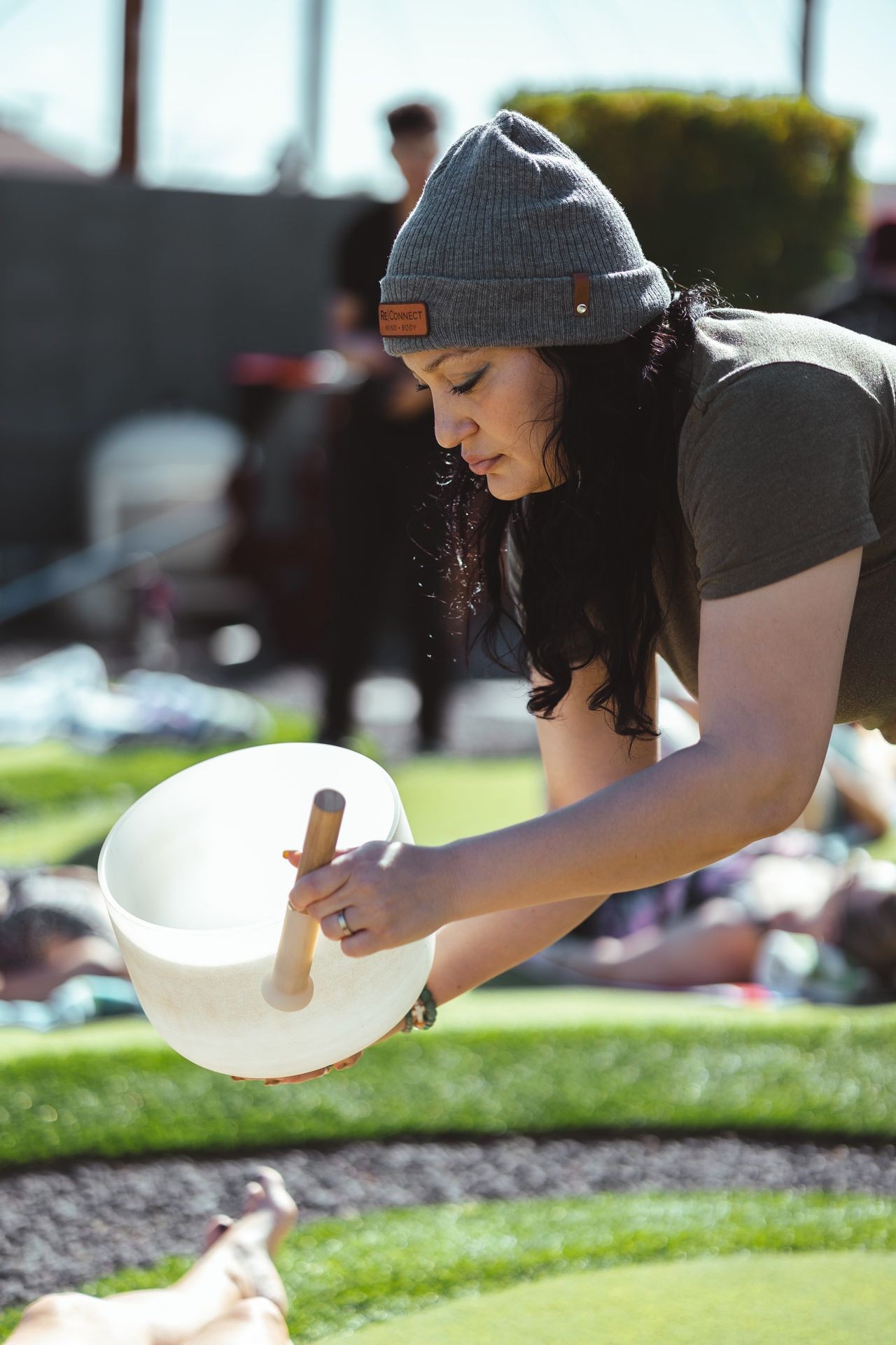 Woman in a beanie playing a crystal singing bowl outdoors on a sunny day.